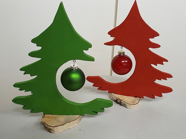 Petits sapins découpés dans du bois avec une boule de Noël suspendue