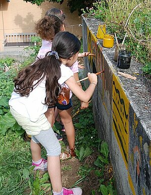 Trois petites filles peignant sur un mur à l'aide de peintures naturelles