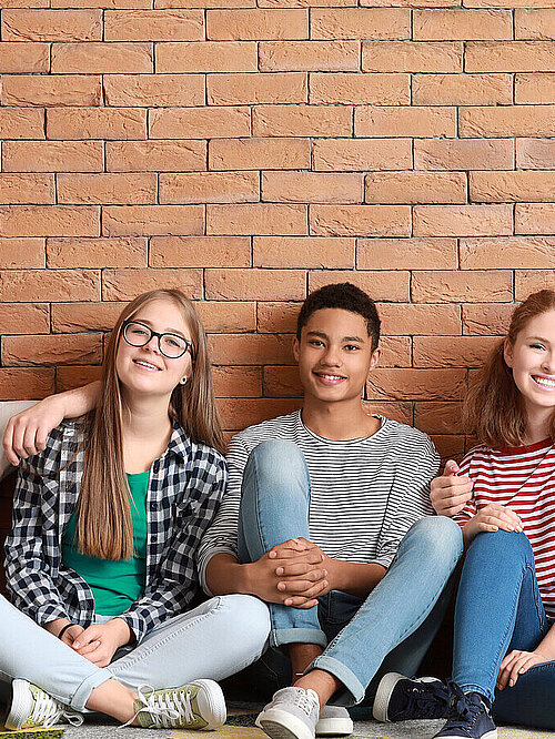 Group of teenagers sitting on floor near brick wall