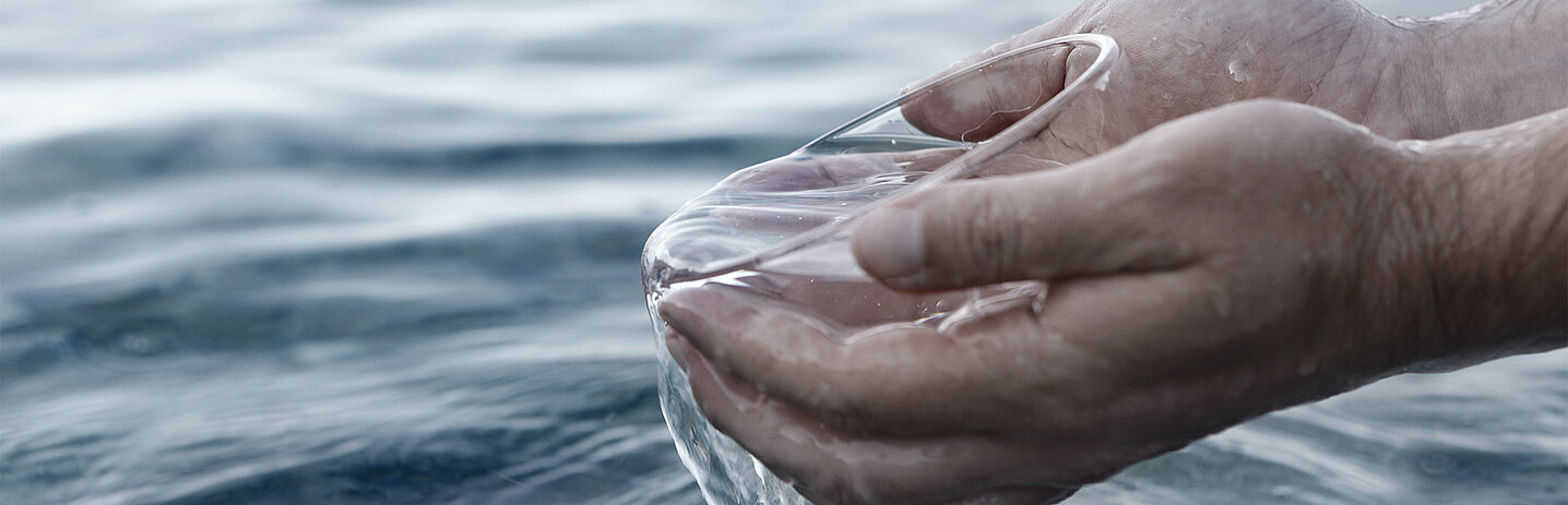 Plan rapproché sur deux mains qui tiennent un bol au-dessus d'une étendue d'eau.