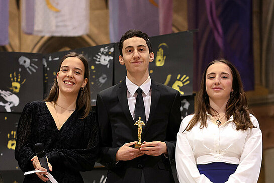 Un jeune reçoit son oscar, entouré de deux accompagnantes.