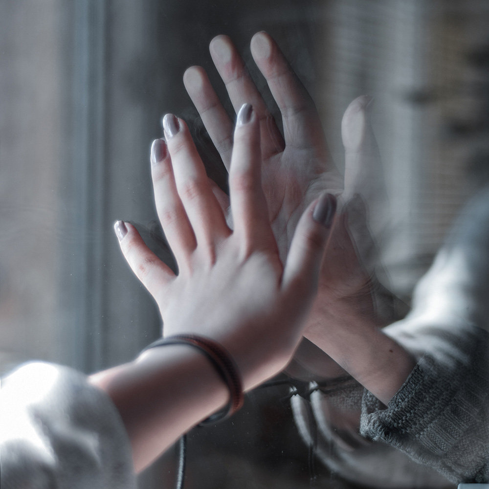 Deux mains qui essaient de se toucher de deux côtés d'une vitre