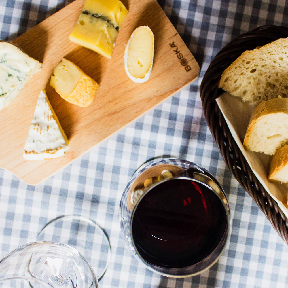 Une planche de fromage, quelques morceaux de pain dans une corbeille et un verre de vin.