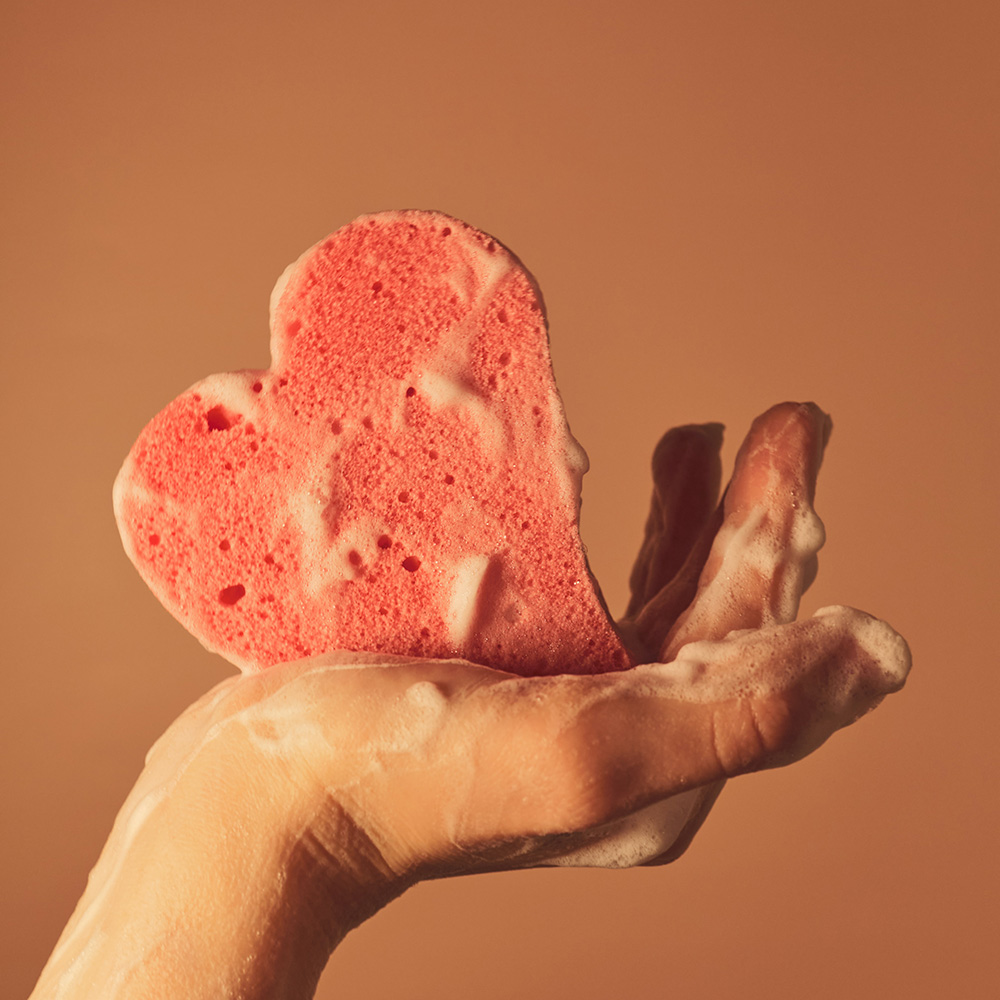 Une éponge en forme de coeur, au creux d'une main savonneuse.