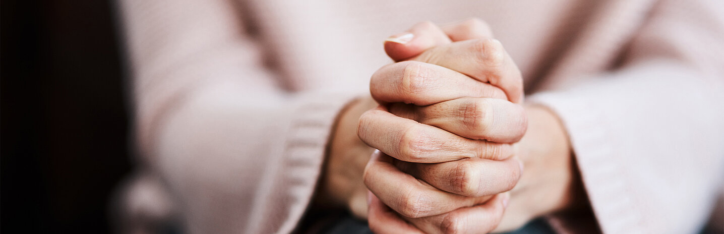 Une femme a les mains jointes en prière.